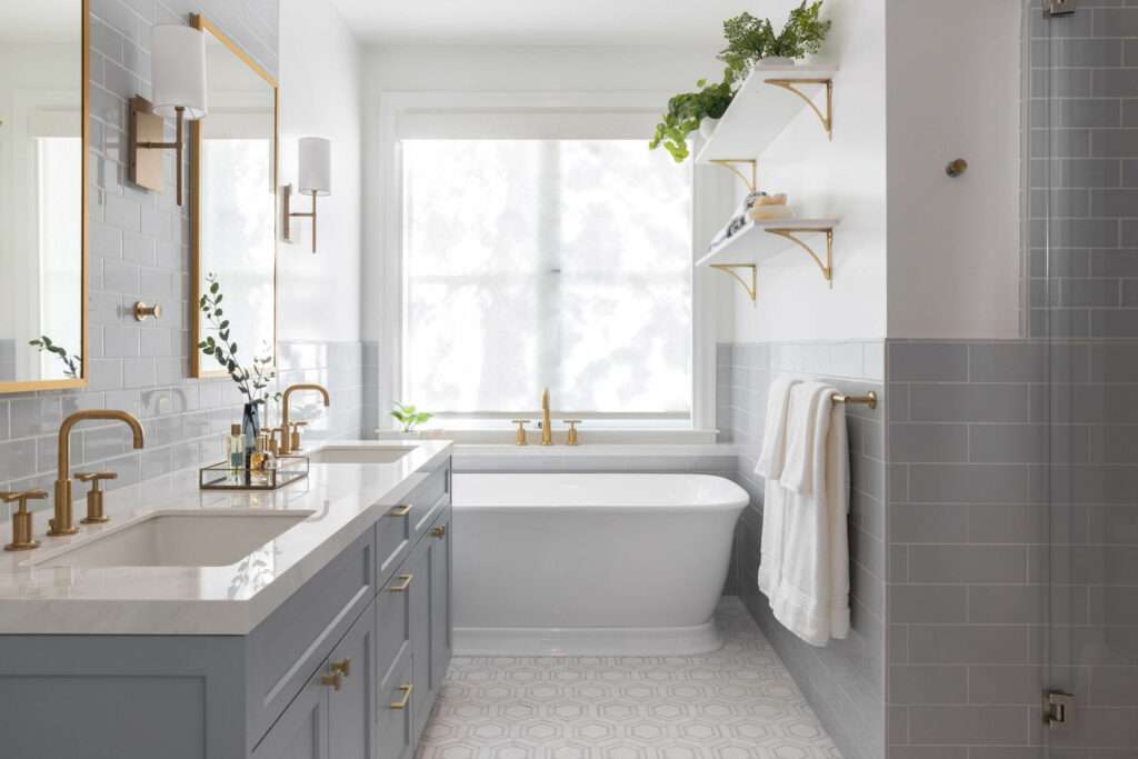 Marin interior designer shares an image of bathroom renovation featuring brass fixtures and muted blue tiles. The free-standing tub is below a large window with beautiful shadows through the sheer window shade.