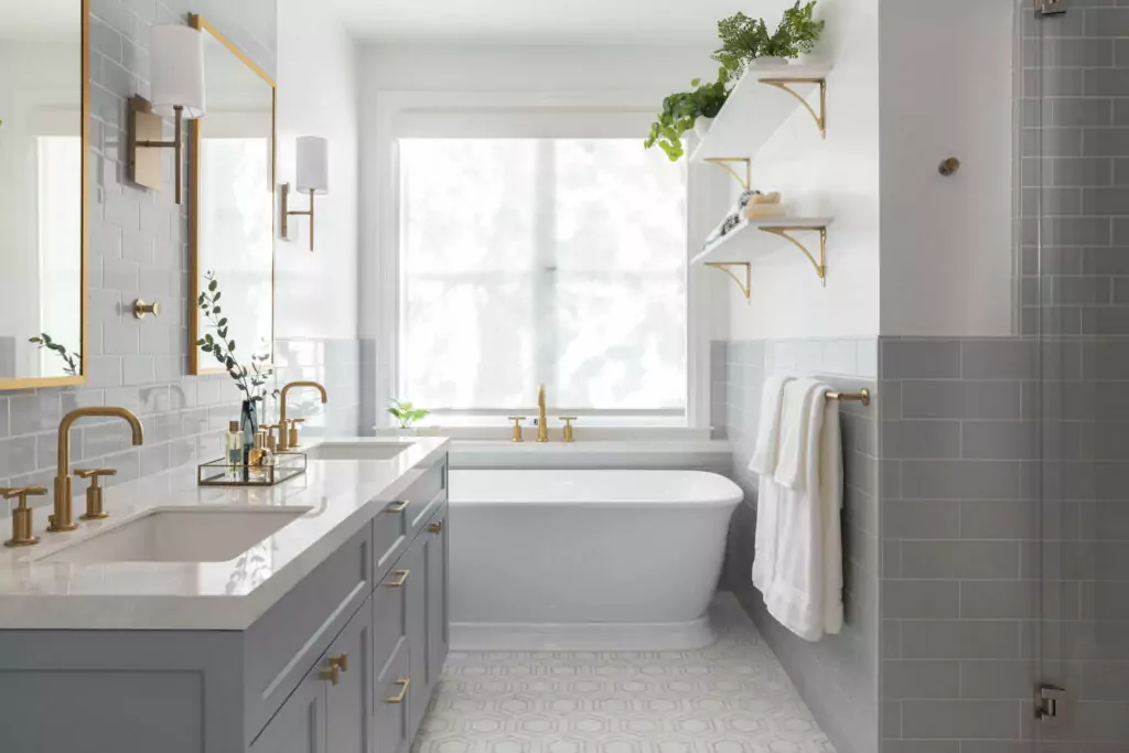 Marin interior designer shares an image of bathroom renovation featuring brass fixtures and muted blue tiles. The free-standing tub is below a large window with beautiful shadows through the sheer window shade. Bathroom renovation design in Sonoma, Marin, Healdsburg, and California Wine Country homes.